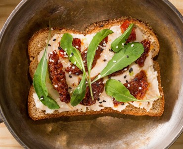 Sanduíche aberto de feijão branco, tomates secos e rúcula