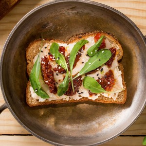 Sanduíche aberto de feijão branco, tomates secos e rúcula